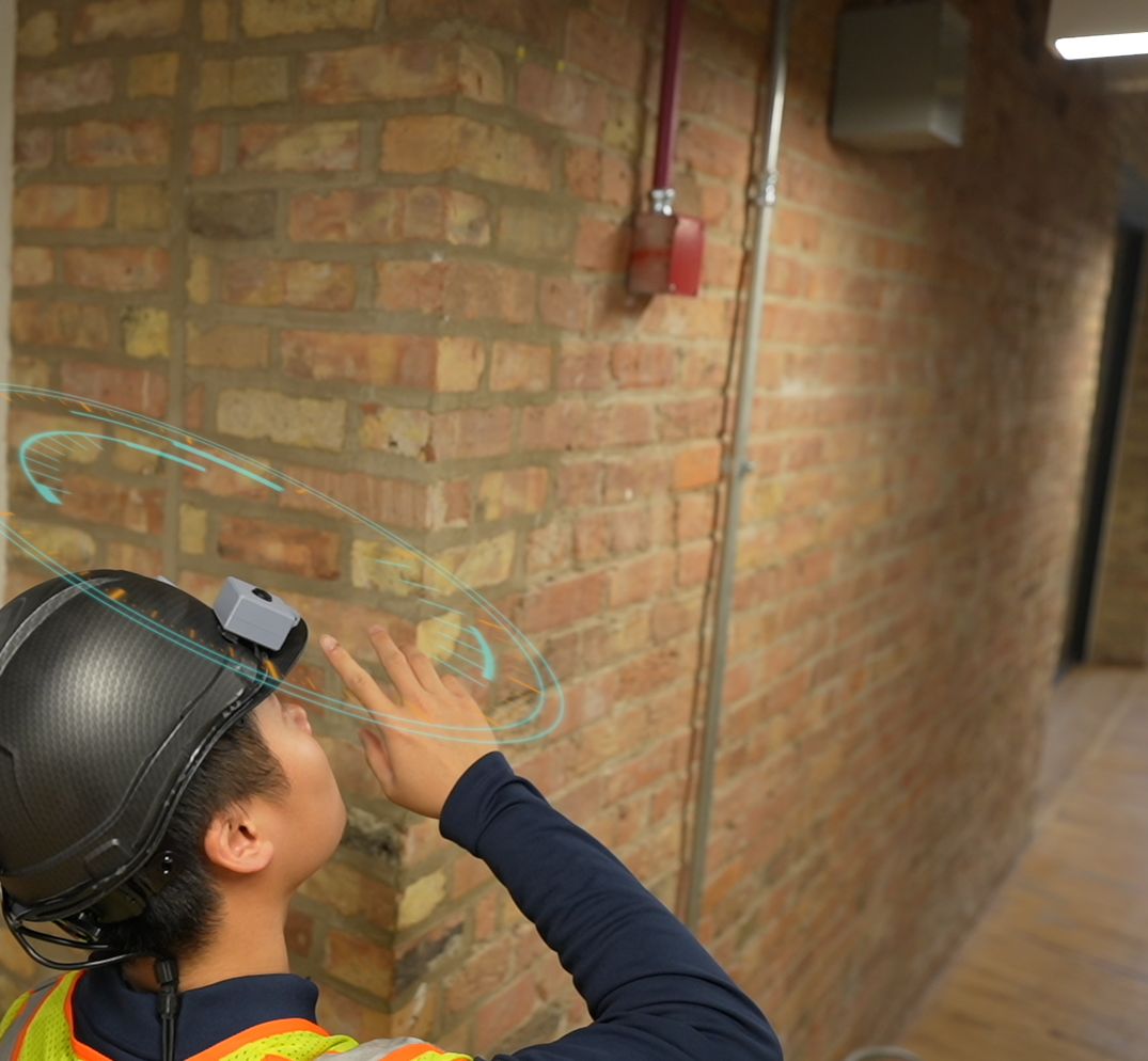 A worker in the helmet reaches toward a brick wall while it scans