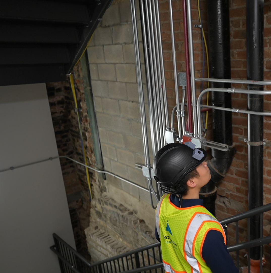 A worker in the helmet captures pipes and conduit in a stairwell