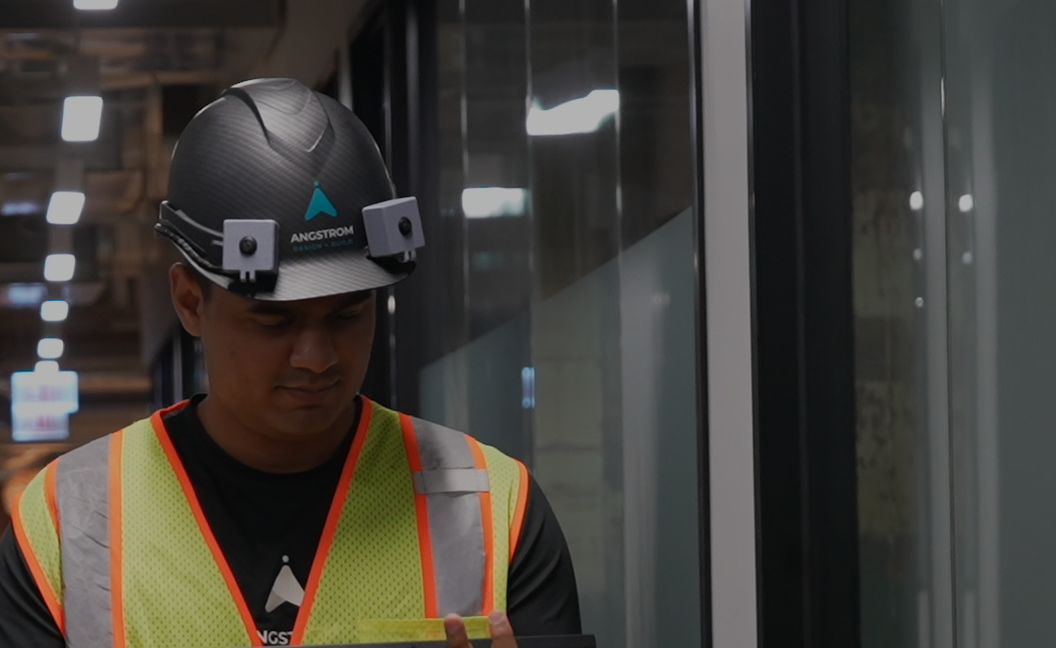 A worker walks a corridor wearing the helmet and holding a tablet
